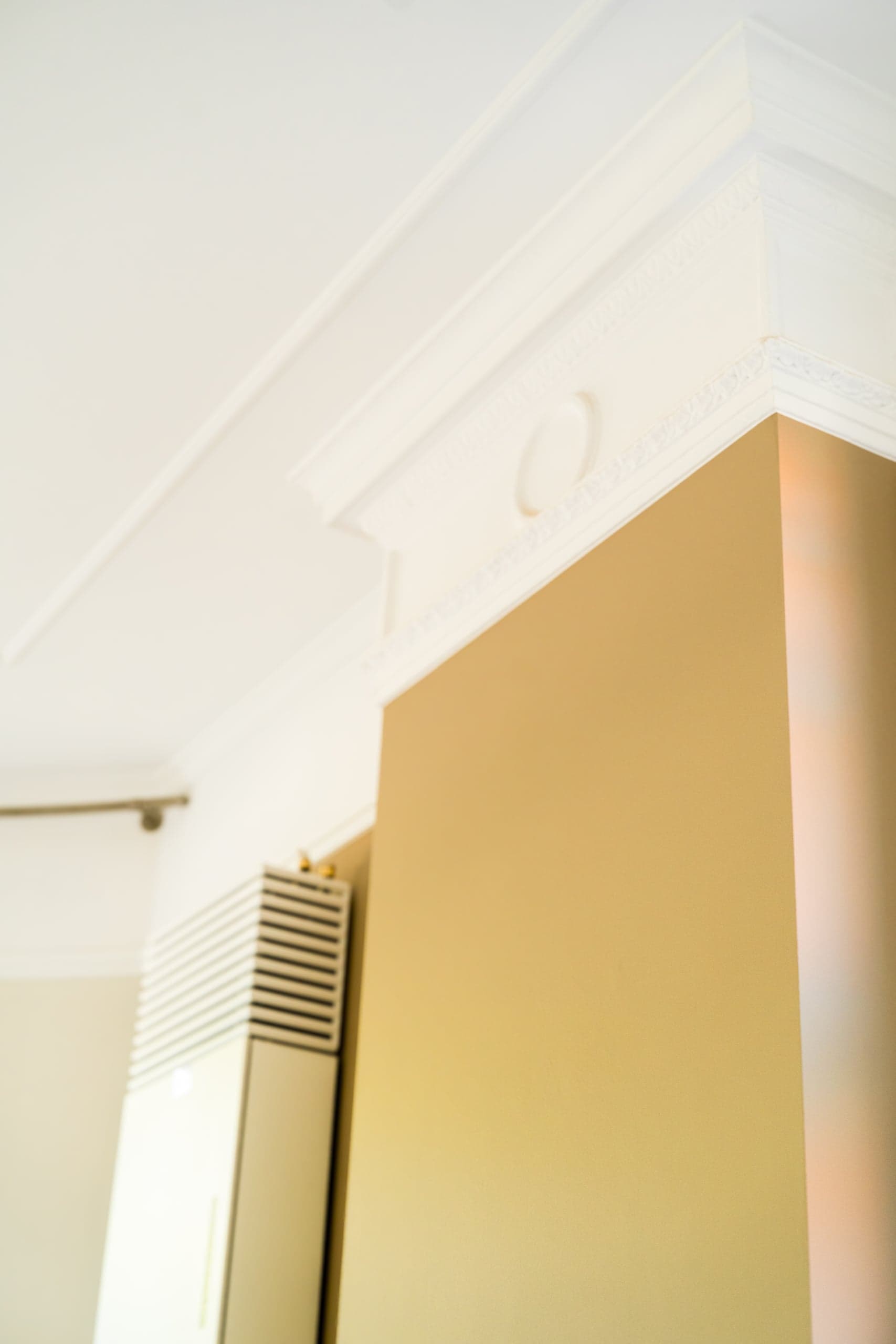 Detail van een strak afgewerkte kroonlijst tegen een gekleurde wand