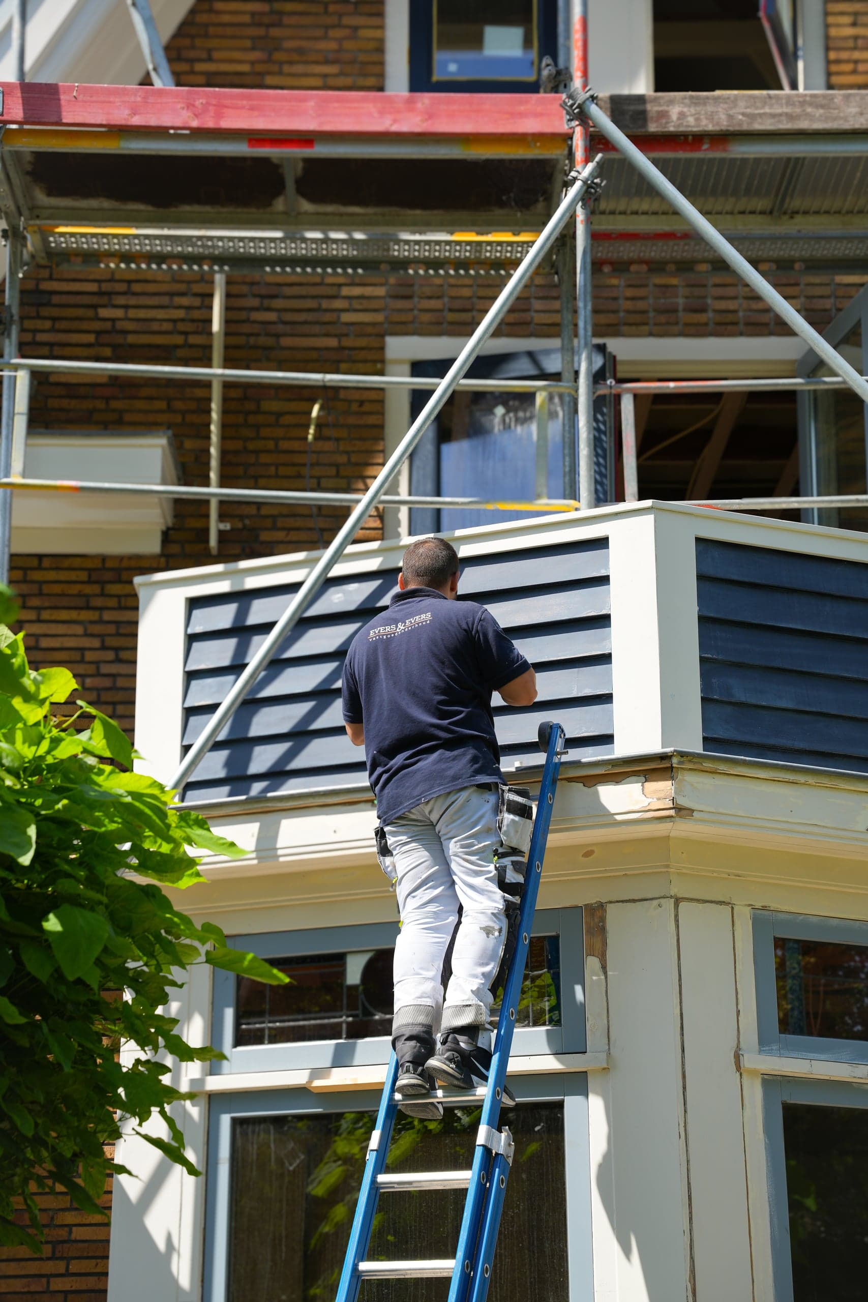 Vakman op een ladder bij de erker van een woonhuis