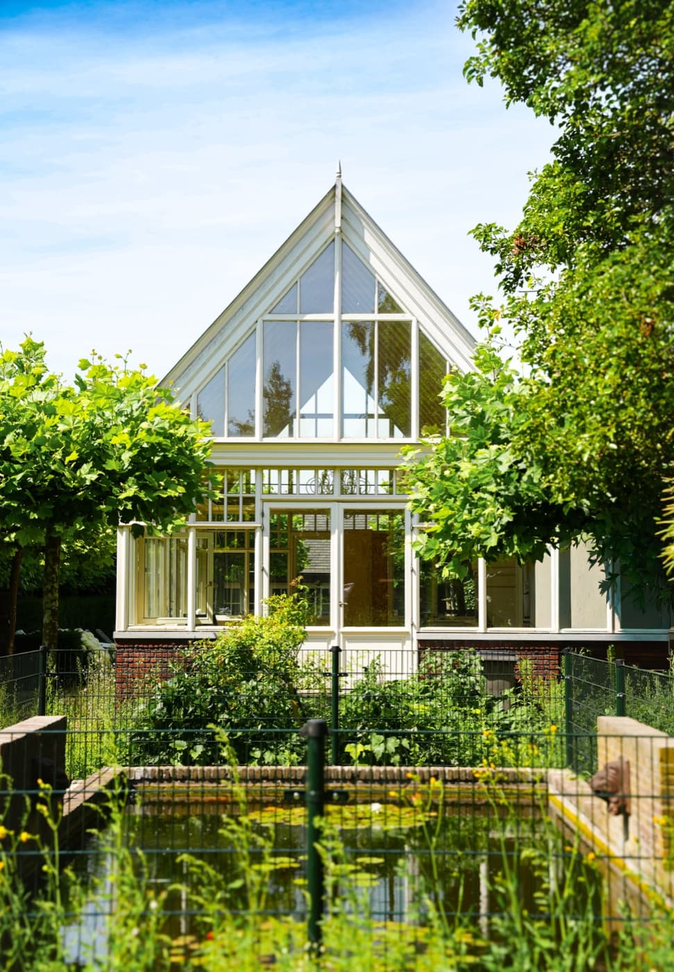 Woning met grote glazen puntgevel achter een tuin met vijver