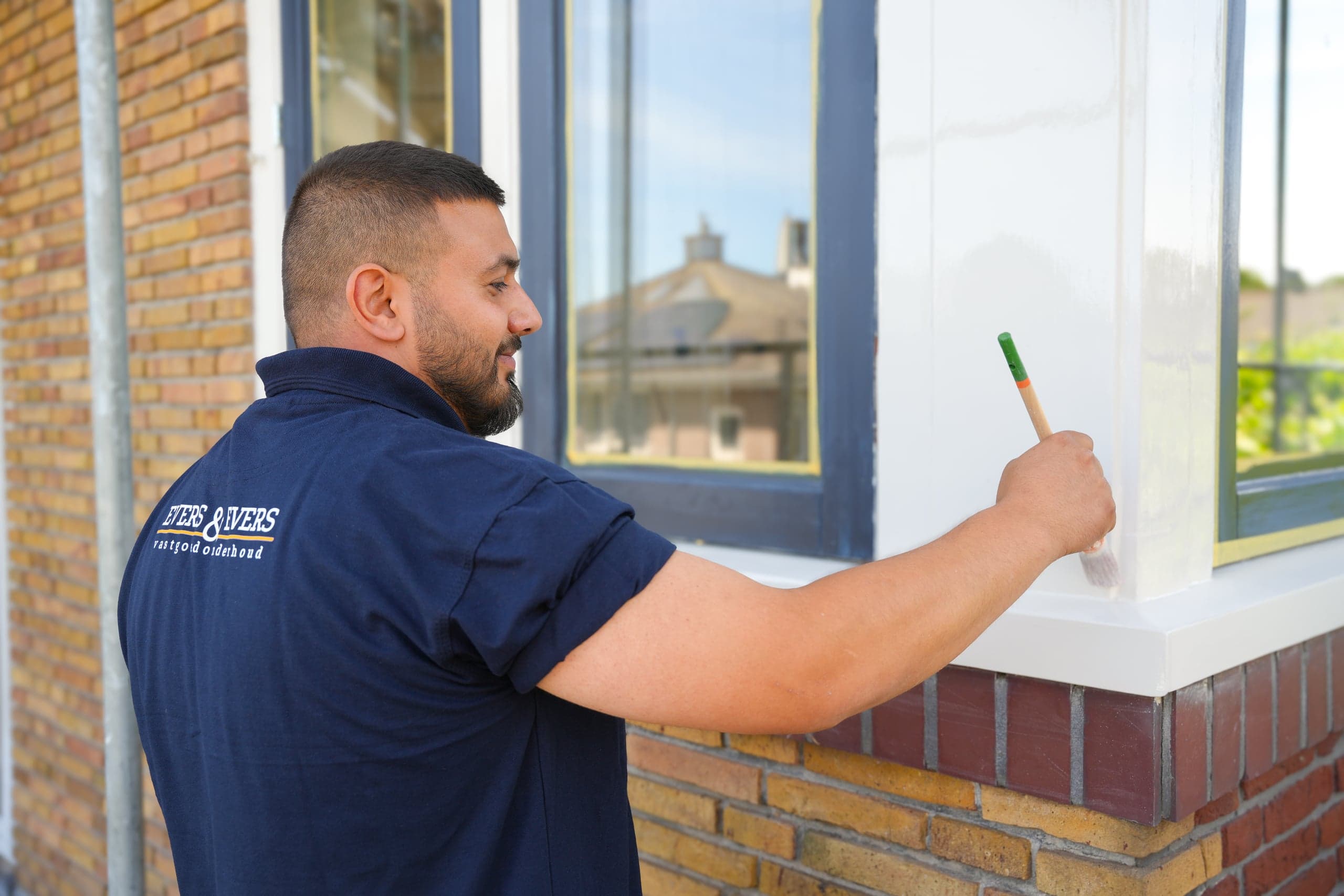 Schilder werkt een houten kozijn af aan de buitenzijde van een woning